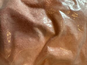 A close-up image shows the texture of pink granular material inside a clear plastic bag with reflective highlights.