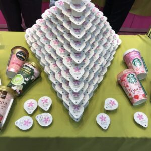 This is a product display featuring a pyramid of Japanese "Japan Flavor" creamers, alongside various ready-to-drink Sakura-themed coffee beverages from brands like Doutor, Excelsior Caffe, and Starbucks.