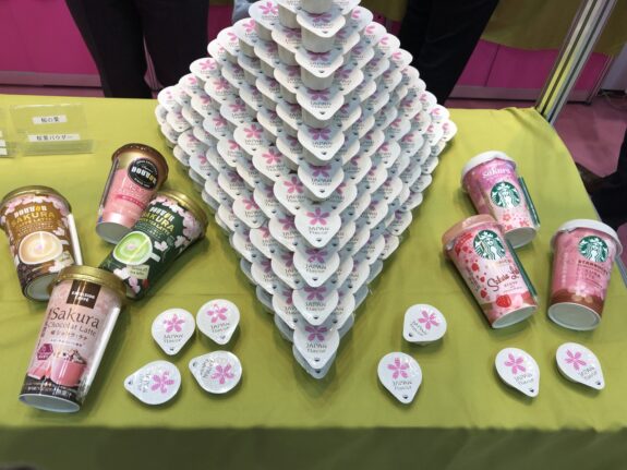 This is a product display featuring a pyramid of Japanese "Japan Flavor" creamers, alongside various ready-to-drink Sakura-themed coffee beverages from brands like Doutor, Excelsior Caffe, and Starbucks.