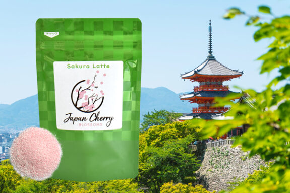 A bag of Sakura Latte mix with a cherry blossom logo stands next to a pile of pink powder against a background of a Japanese pagoda and mountains.