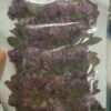 This image displays a collection of dried, pressed purple flowers and green leaves sealed in a clear plastic package.