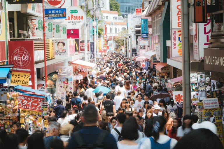 This image captures a densely packed street scene in Japan, filled with a multitude of people walking amidst a variety of shops and colorful signs.