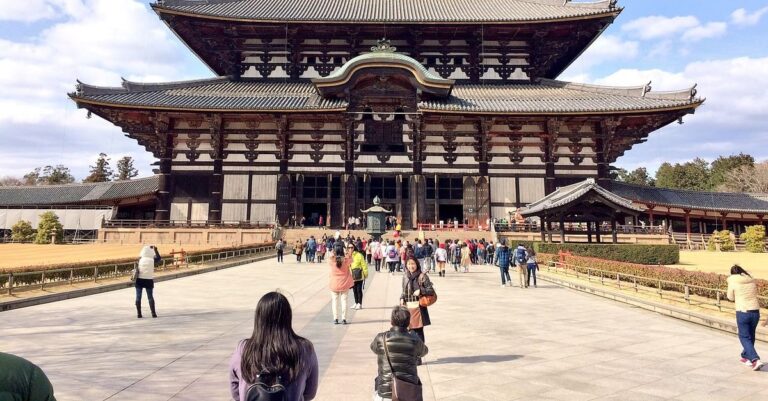 A wide shot shows many tourists visiting the historic Todai-ji Temple in Nara, Japan on a bright, partly cloudy day.