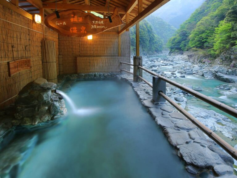 An outdoor hot spring with a view of a river and mountains.